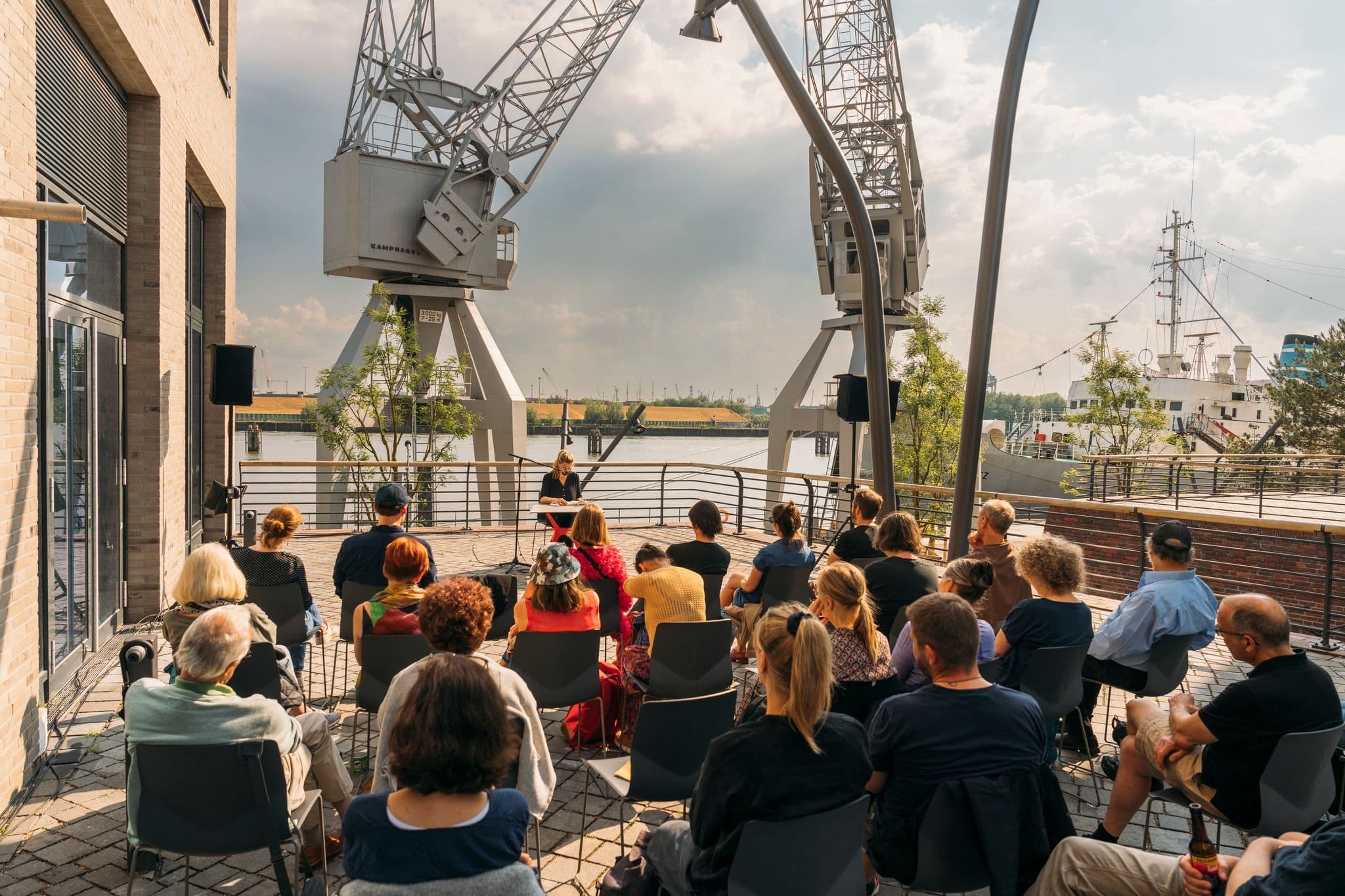 Personen sitzen im Publikum und eine Person liest etwas vor.